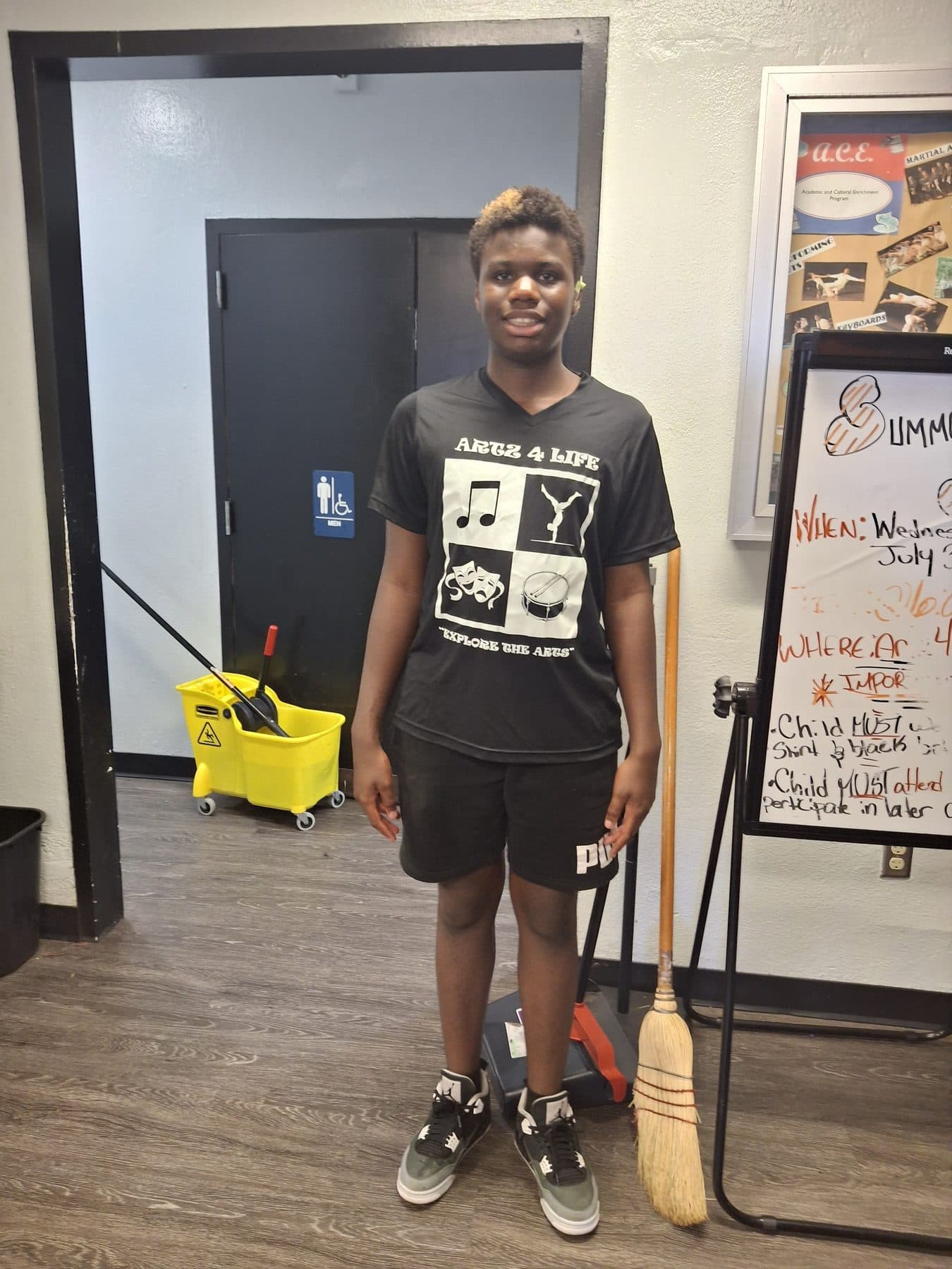 A student ready to begin a facilities task with a broom and mop bucket