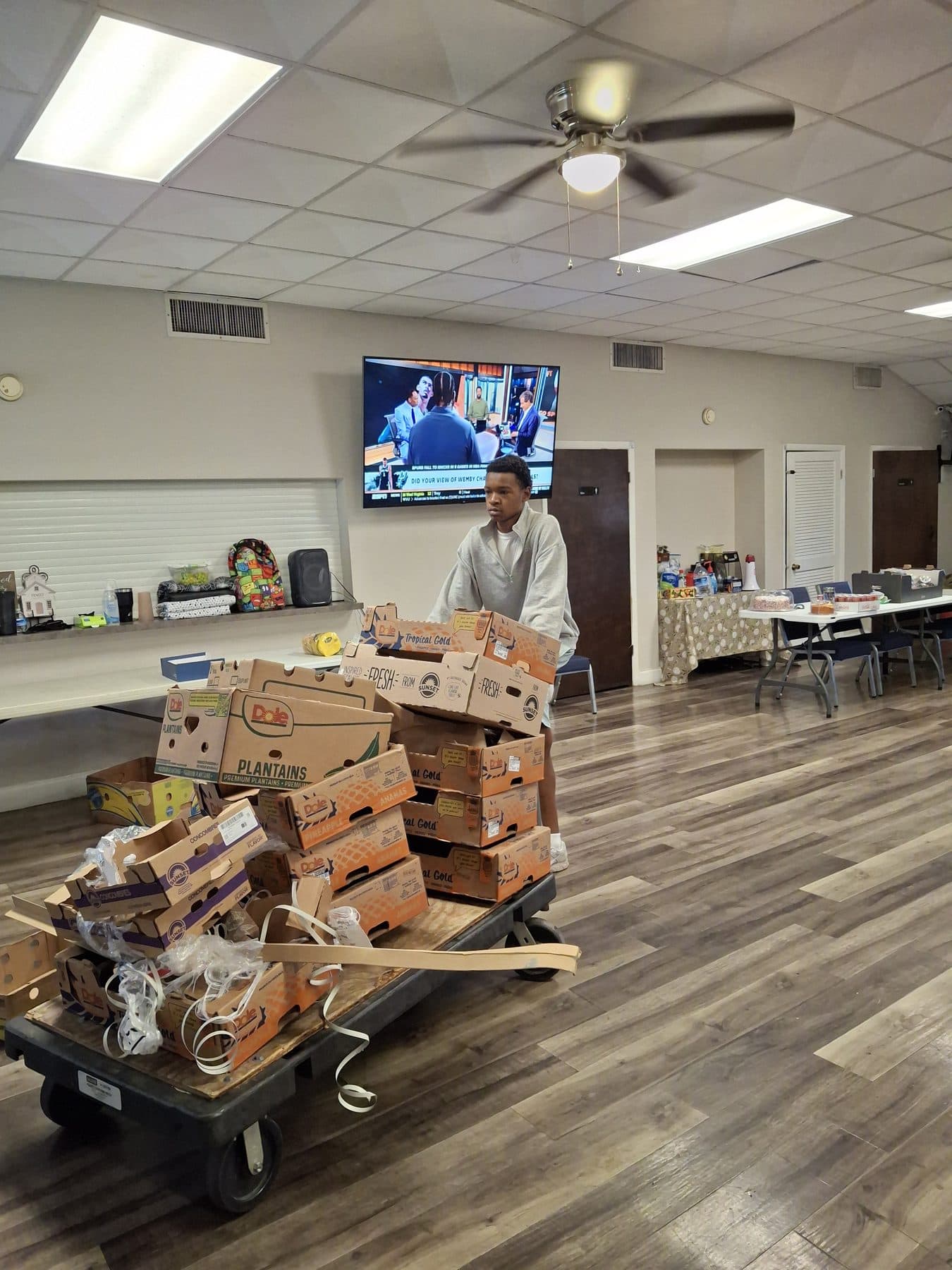 A participant helping run a community food distribution, produce boxes staged on a cart